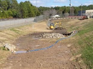 Stormwater detention basin under maintenance with exposed soil, riprap placement, and excavation equipment working on sediment removal and erosion control.